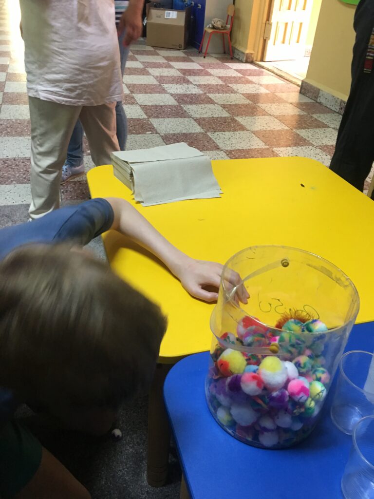 Na stoliku pojemnik z kolorowymi kulami. Dziecko szuka niespodzianki w nim ukrytej
