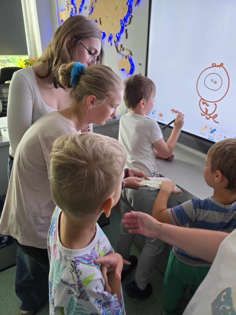 Sala lekcyjna, dzieci cos piszą przy monitorze dotykowym.