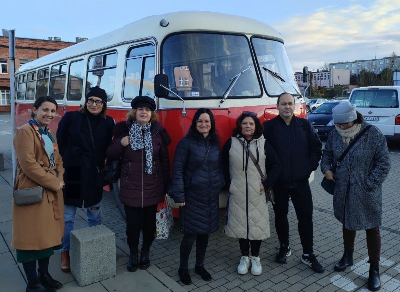 Osoby stoją przed czerwonym starym autobusem.