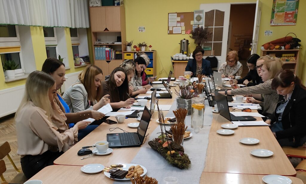 Ludzie siedzą wokół stołu  i pracują na laptopach. 